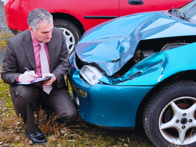 Man in suit writing a report of a car accident while looking the car damage. Undervalue Houston Car Accident Claims